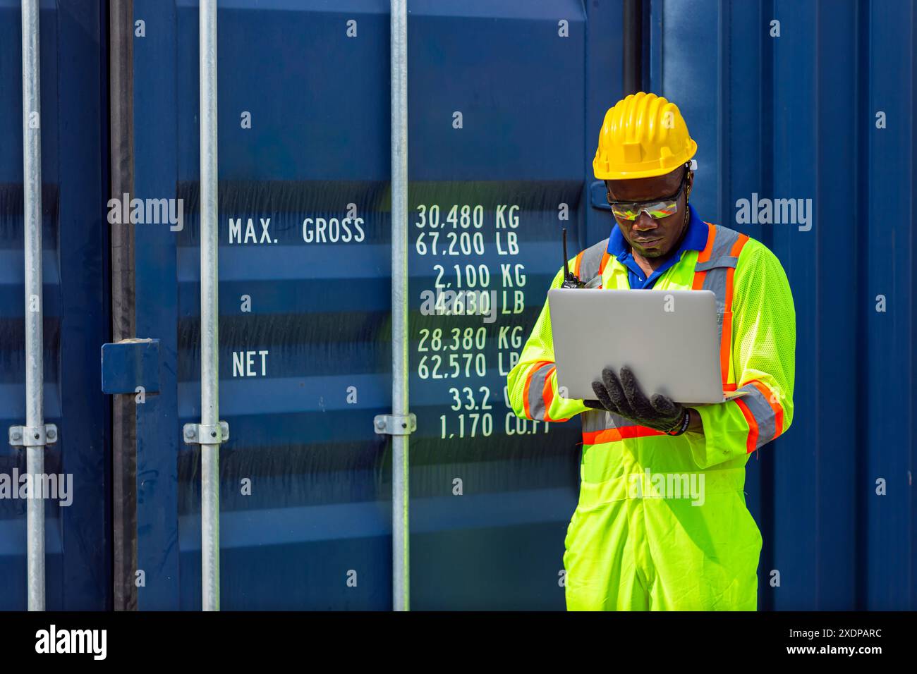 Lavoratore nero africano nel porto di carico Shipping Industrial in Yellow Hard Hat Safety Vest on Duty. Caposquadra o supervisore nel terminal di imbarco delle navi container. Foto Stock