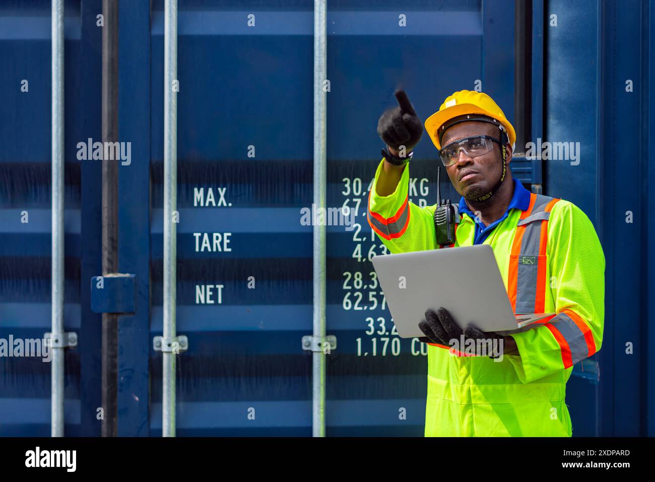 Lavoratore nero africano nel porto di carico Shipping Industrial in Yellow Hard Hat Safety Vest on Duty. Caposquadra o supervisore nel terminal di imbarco delle navi container. Foto Stock