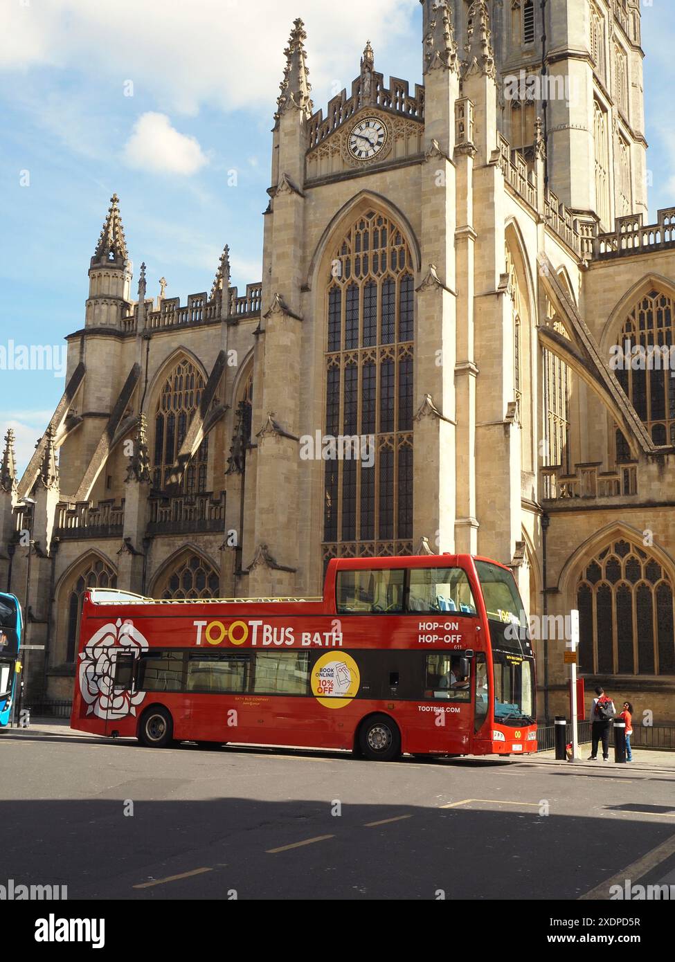 Tour guidati Hop-On Hop-Off della città con autobus Toot Bus con persone che salgono e lasciano l'autobus e l'abbazia di Bath sullo sfondo. Bath, Somerset, Regno Unito Foto Stock