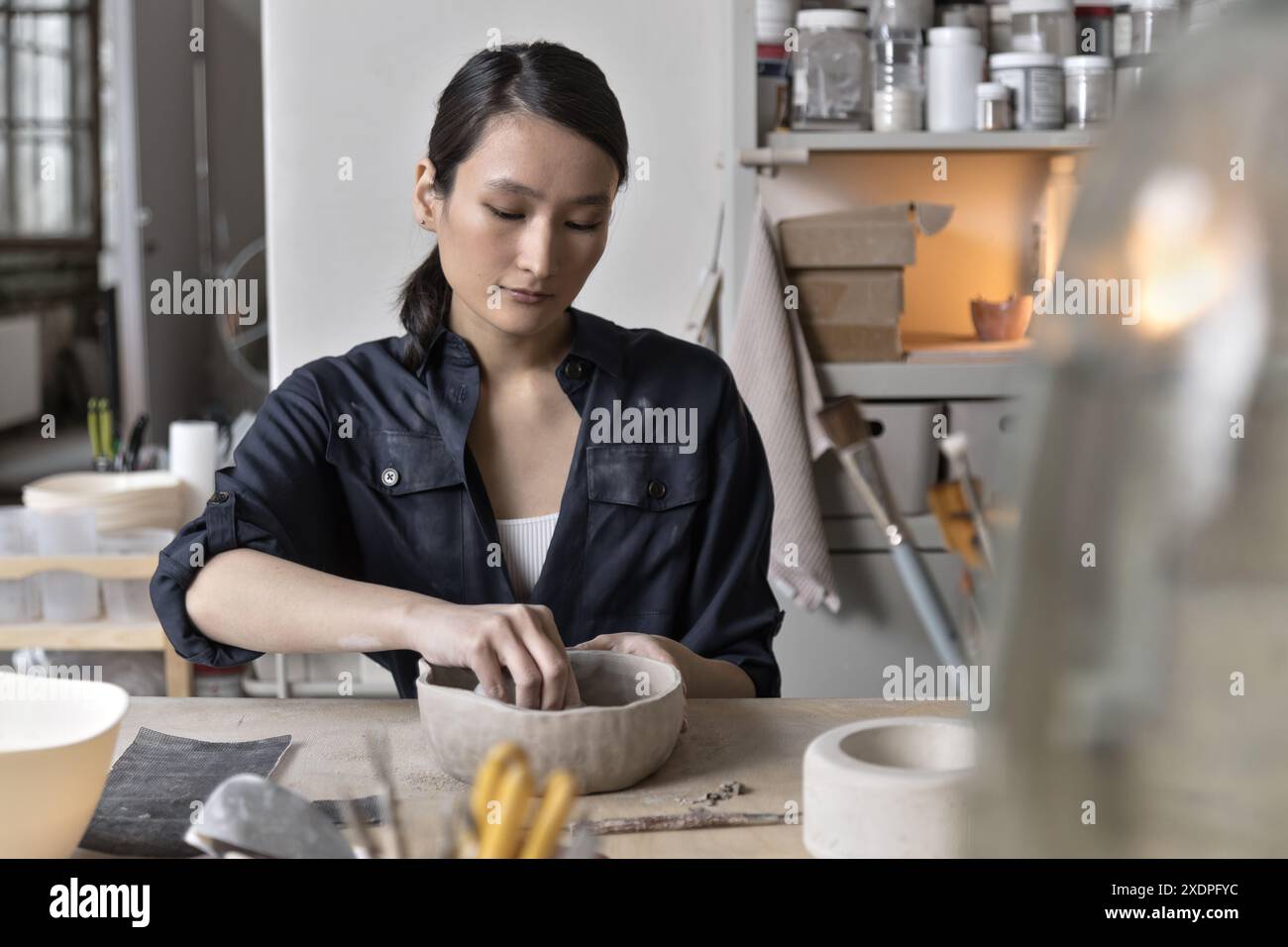 Artista asiatico lavora a un tavolo di lavorazione in uno studio di ceramica Foto Stock