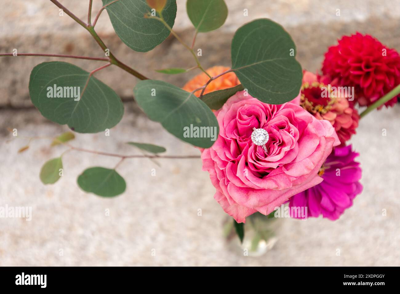 Anello di diamanti accoccolato in un vivace bouquet di fiori e foglie miste Foto Stock