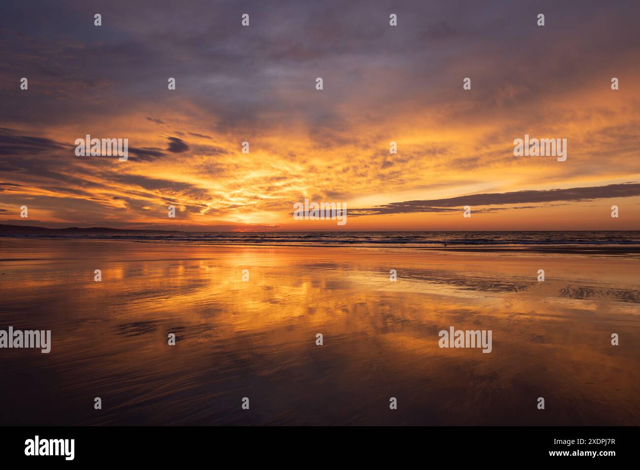 Tramonto dorato su una spiaggia tranquilla con riflessi sulla sabbia bagnata Foto Stock
