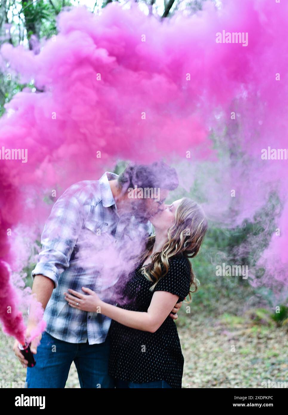 Coppia che si baciano in mezzo al fumo rosa in un ambiente forestale. Foto Stock