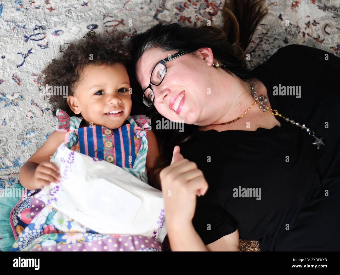 Donna e ragazza sdraiate su un tappeto a motivi geometrici, sorridenti, con salviette in mano. Foto Stock