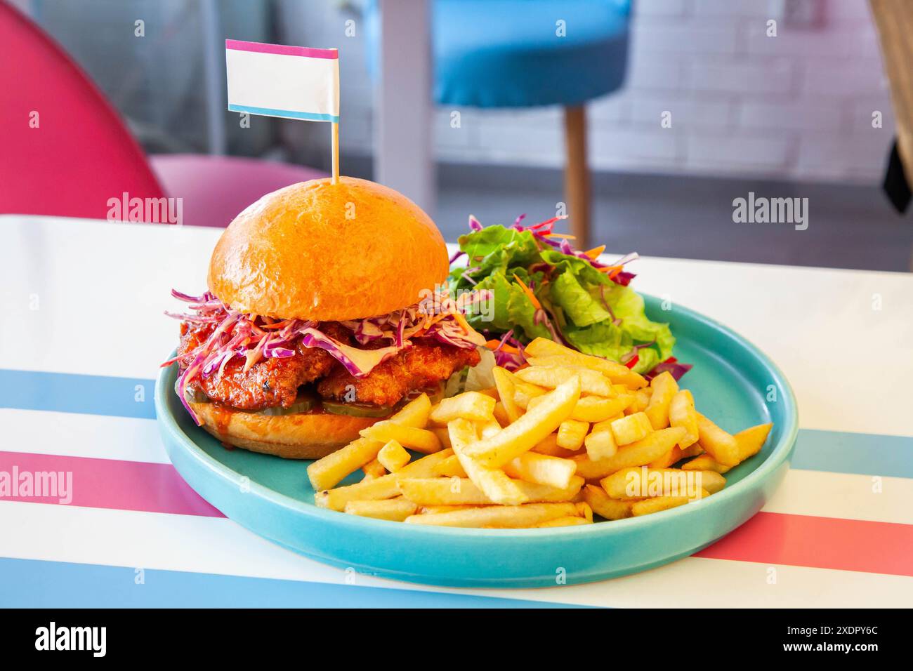 Hamburger di pollo fritto glassato al miele in panino brioche servito con patatine fritte e insalata su un piatto in un ambiente caffetteria. Foto Stock