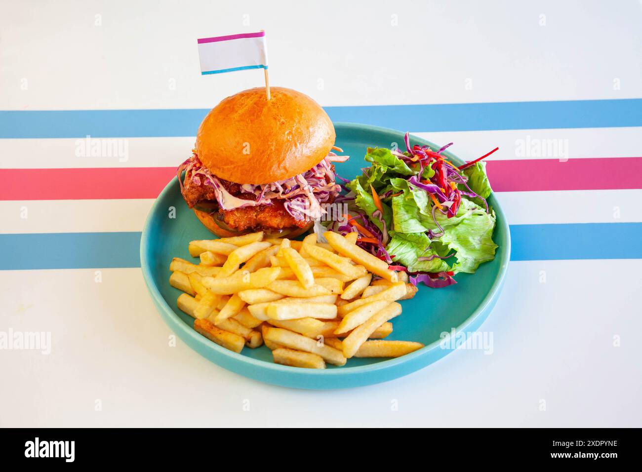 Hamburger di pollo fritto glassato al miele in panino brioche servito con patatine fritte e insalata su un piatto in un ambiente caffetteria. Foto Stock