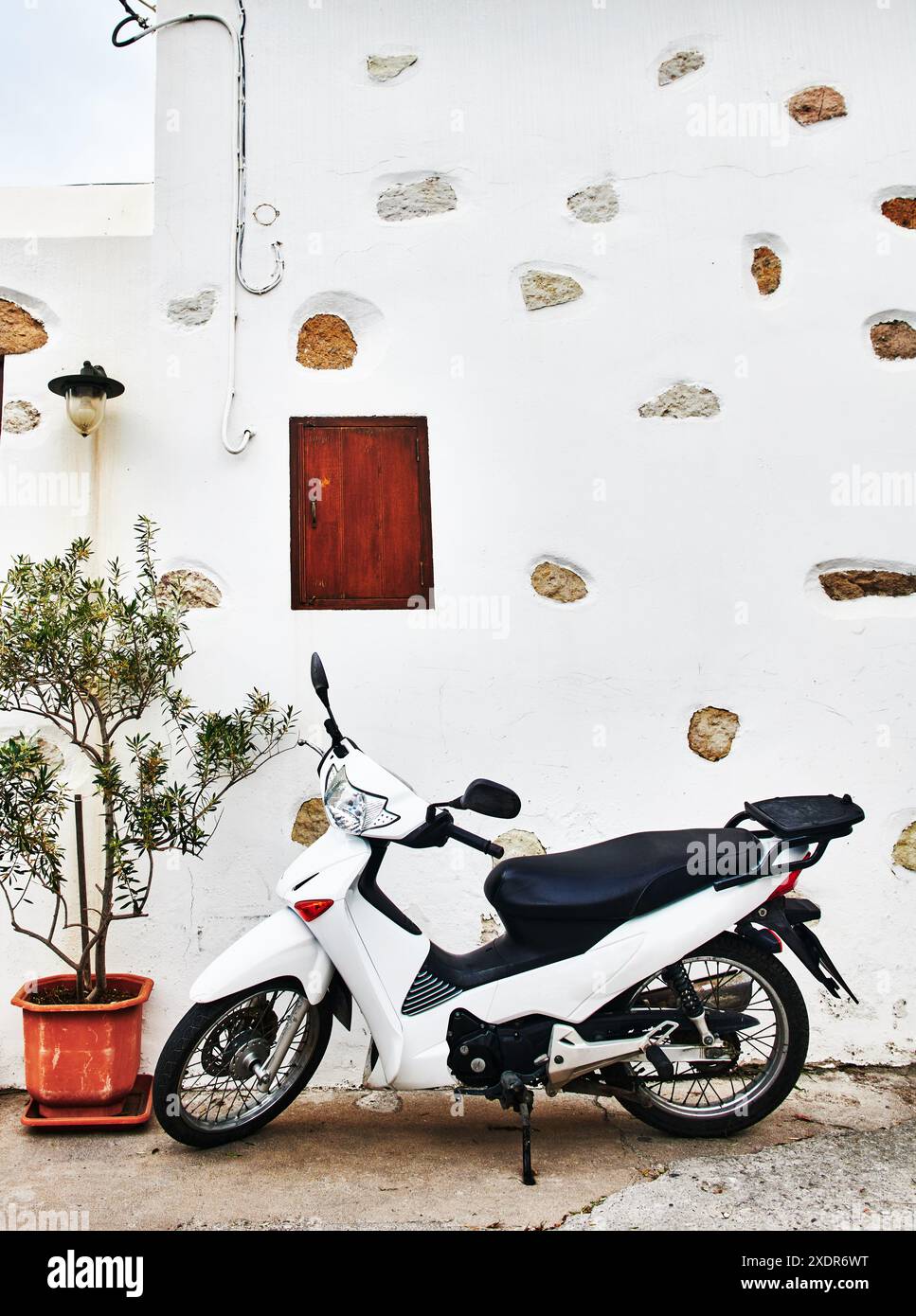 Moto bianca in piedi contro un muro di pietra bianca a Patmos, Grecia, Isole greche, Europa Foto Stock