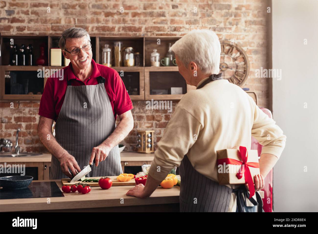 Una coppia senior che ama cucinare insieme in cucina con un regalo a sorpresa Foto Stock