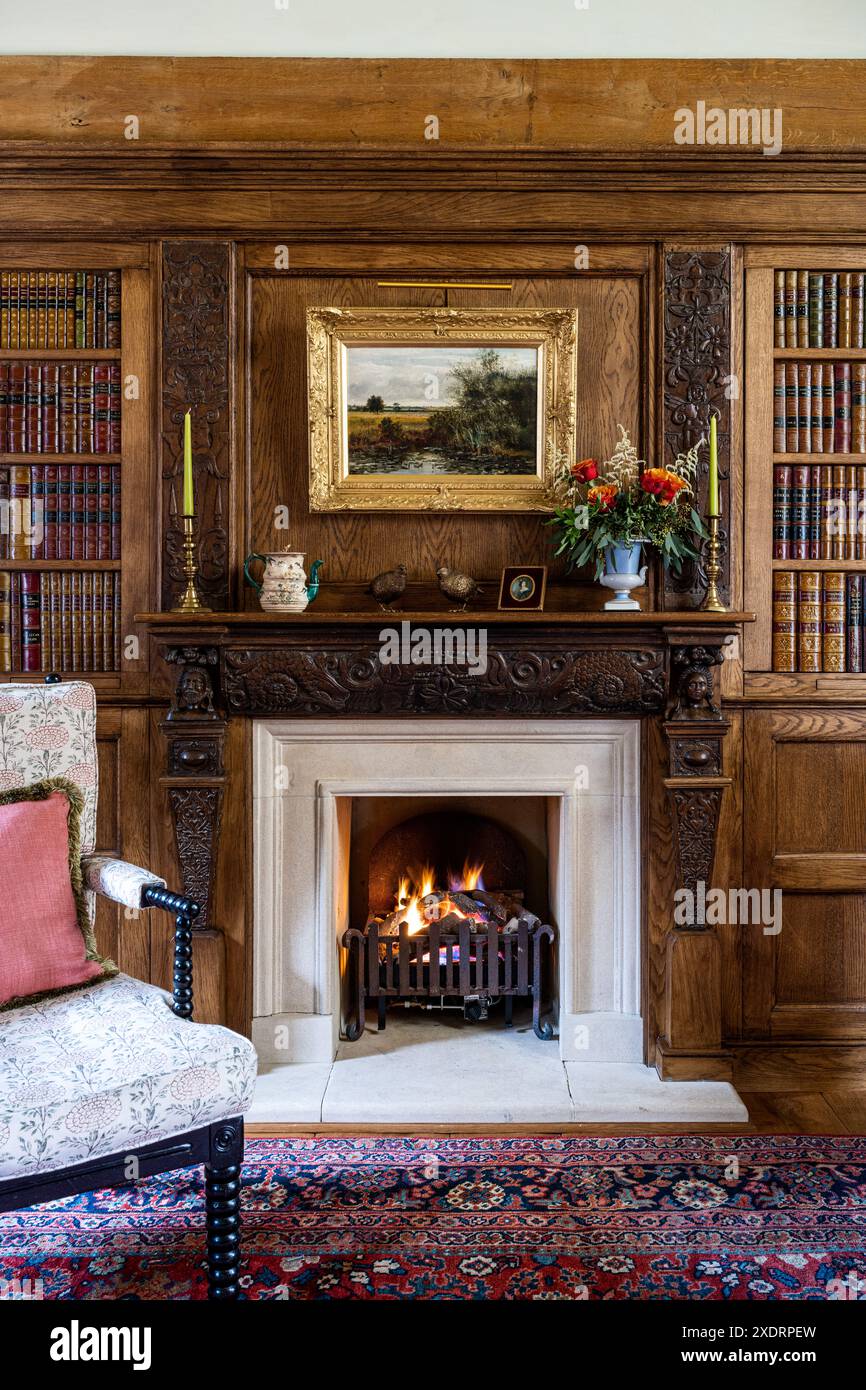 Fuoco acceso e librerie nell'estensione della biblioteca della fattoria Tudor del XVI secolo, Hertfordshire, Inghilterra, Regno Unito Foto Stock