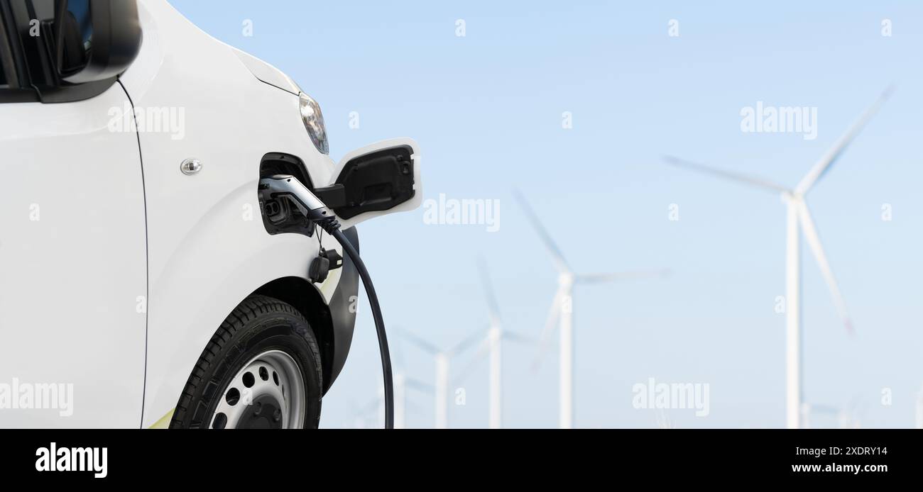 Ricarica di furgoni elettrici e turbine eoliche in background Foto Stock