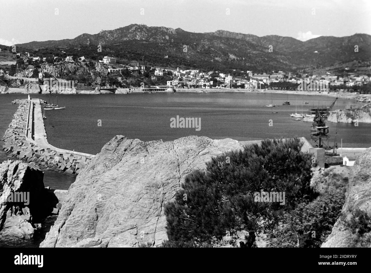 Blick über die Bucht von San Felíu de Guixols, rechts der Kran zur Verladung von Korkplatten, Links der Kai der Sportsmarina mit Yachten, Katalonien 1957. Vista sulla baia di San Felíu de Guixols, sulla destra la gru per caricare lastre di sughero, sulla sinistra la banchina del porticciolo sportivo con yacht, Catalonia 1957. Foto Stock