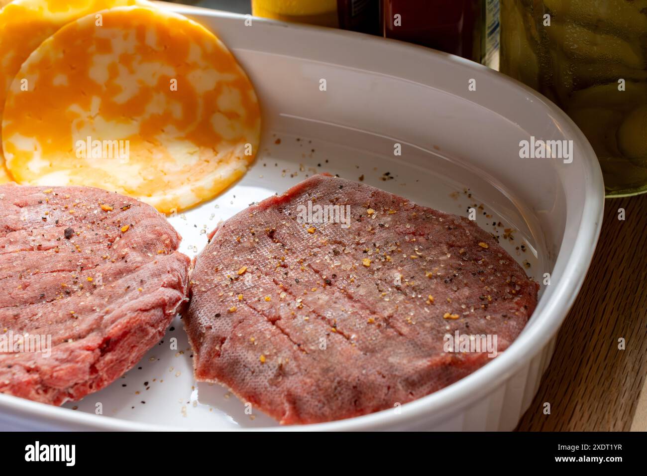 Due hamburger di manzo surgelati con condimenti e fette di formaggio cojack. Il grill si sta preriscaldando. Foto Stock