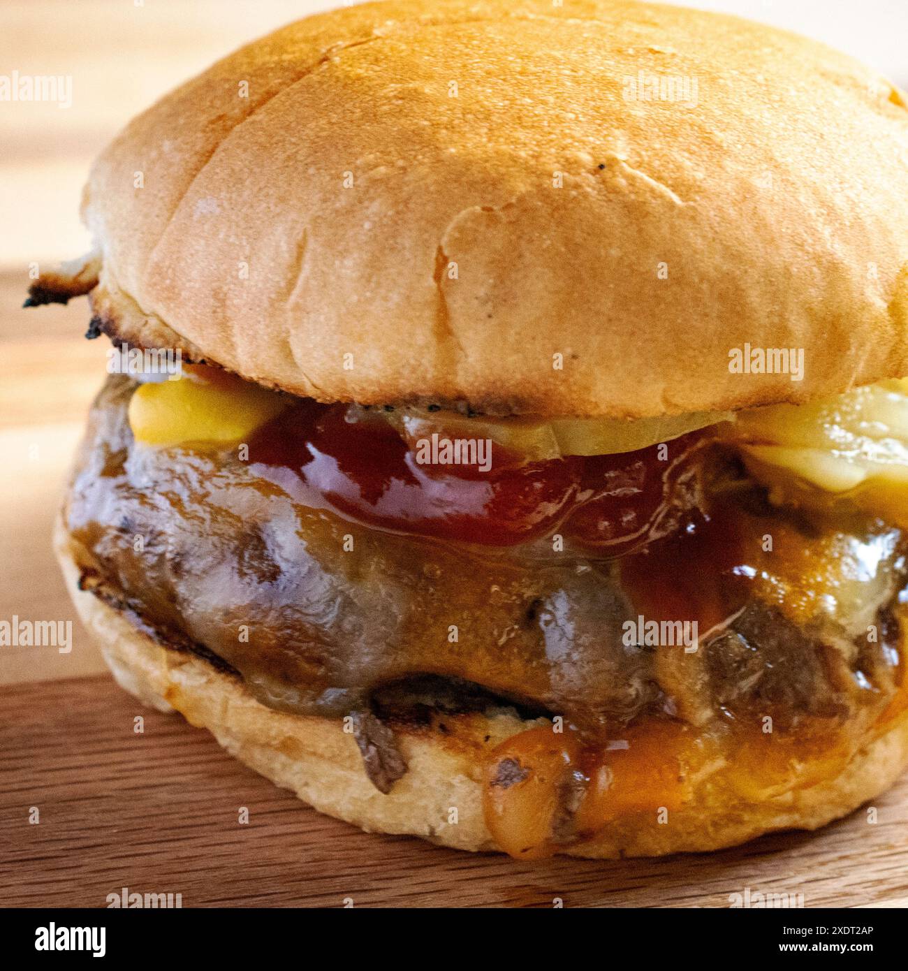 Direttamente dalla griglia, hamburger con formaggio cojack, cipolle grigliate, sottaceti di aneto, ketchup e senape su un panino tostato. Su un boa di legno Foto Stock