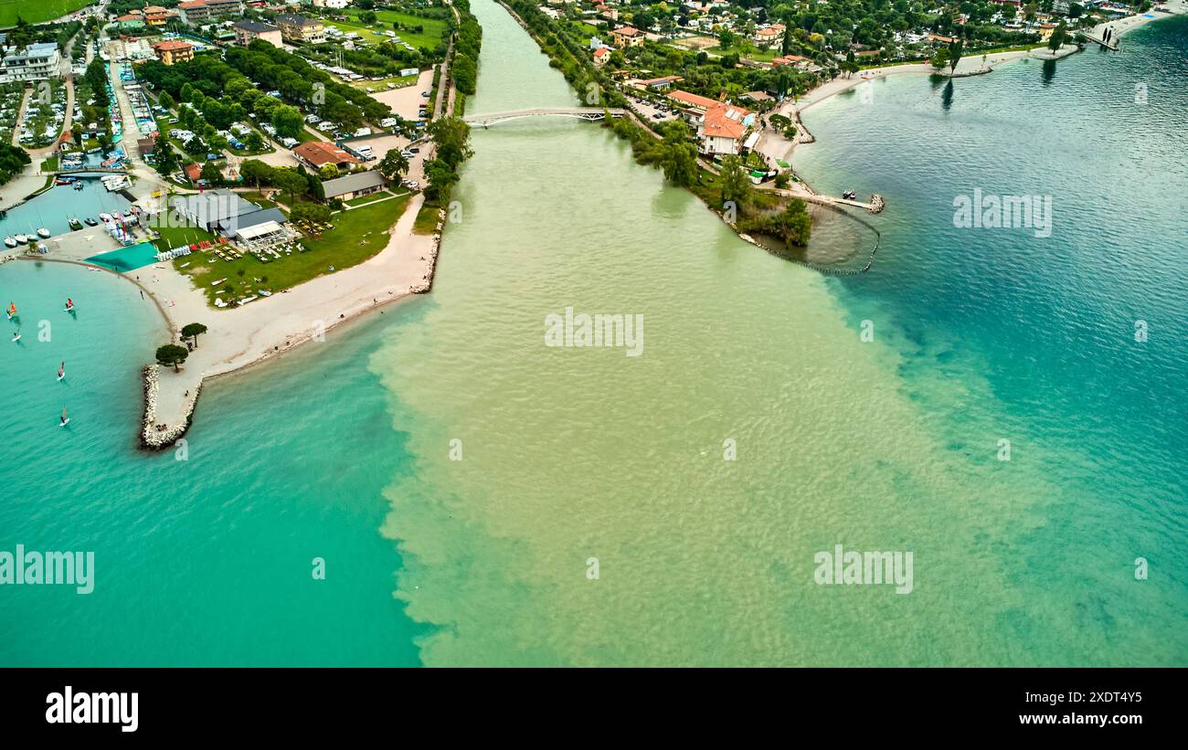 Nago Torbole, Garda, Italia - 24 giugno 2024: L'acqua fluisce dal fiume Sarca al Lago di Garda nella località di villeggiatura settentrionale di Torbole dopo persistenti piogge e tempeste. Il lago ha un alto livello d'acqua il lago ha un alto livello d'acqua. Veduta aerea del fiume Sarca nella città settentrionale di Torbole sul Lago di Garda *** Wassermengen fließen im nördlichen Urlaubsort Torbole vom Fluss Sarca nach anhaltenden Regenfällen und Unwetter in den Gardasee. Vedi HAT hohen Pegelstand. Luftaufnahme vom Fluss Sarca im nördlichen Ort Torbole am Gardasee Foto Stock