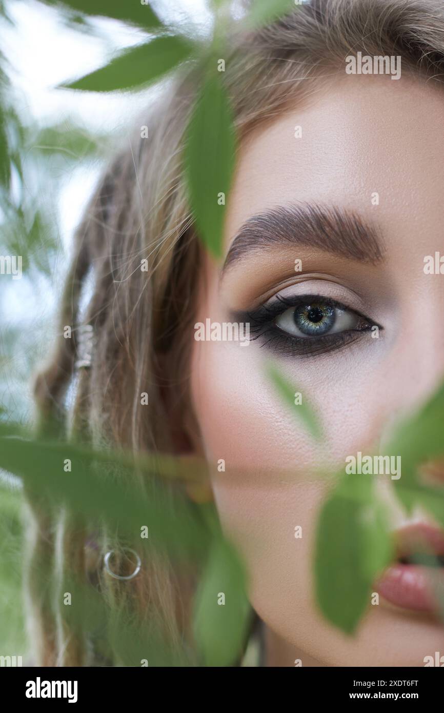 Foto ravvicinata di un occhio femminile che sbircia attraverso il verde fogliame, l'immagine cattura un senso di mistero e intrigo. Foto Stock