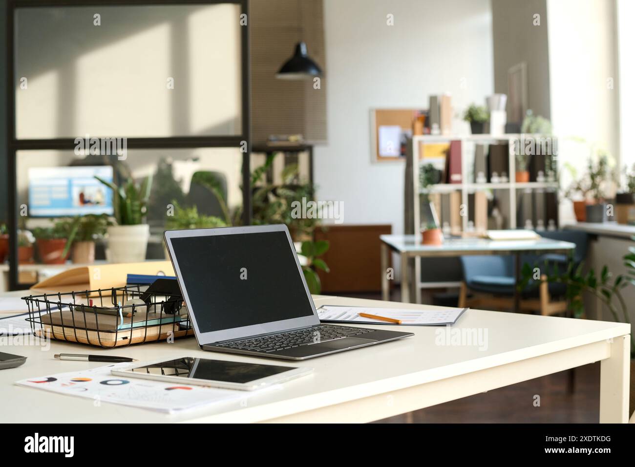 Immagine di sfondo degli interni di un ufficio open space illuminato dal sole con laptop sulla scrivania del luogo di lavoro in primo piano, spazio di copia Foto Stock