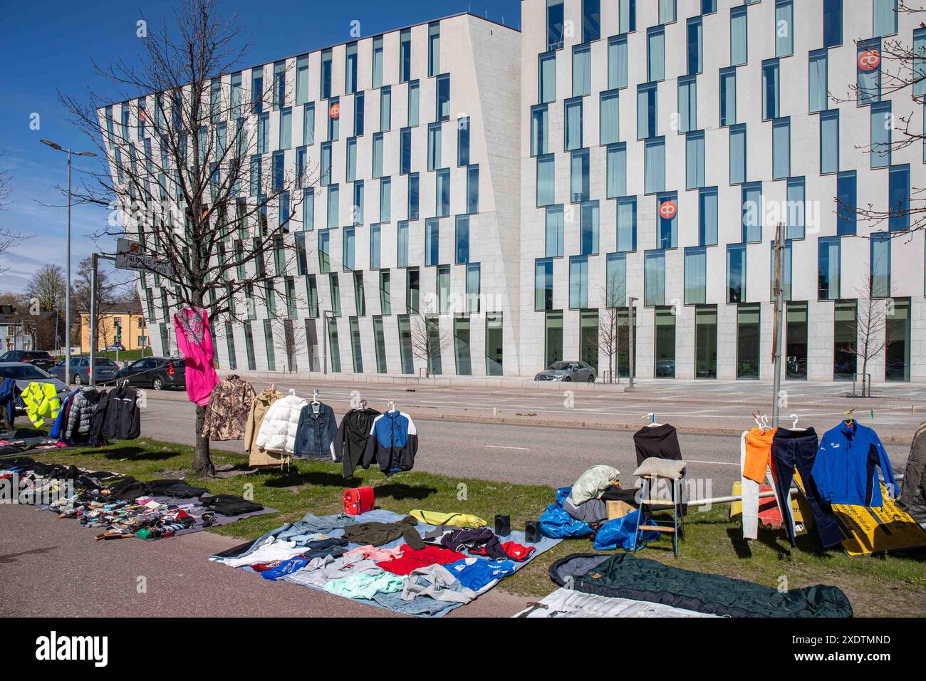 Articoli usati, principalmente vestiti, in vendita al mercato delle pulci pop-up all'aperto del Dallapé Park. La sede centrale del gruppo OP in background. Vallila, Helsinki, Finlandia. Foto Stock