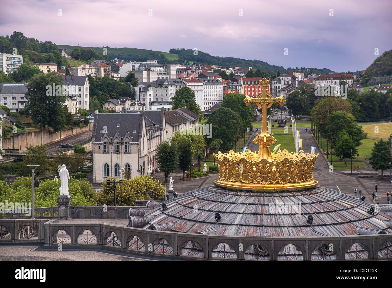 Croce dorata in cima a una cupola della chiesa e vista della città di Lourdes in lontananza Foto Stock