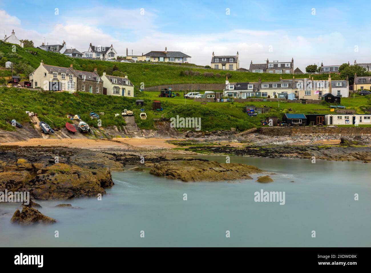 Il pittoresco Collieston Harbour nell'Aberdeenshire, Scozia, presenta affascinanti cottage annidati contro aspre scogliere, che si affacciano su un piccolo riparato Foto Stock