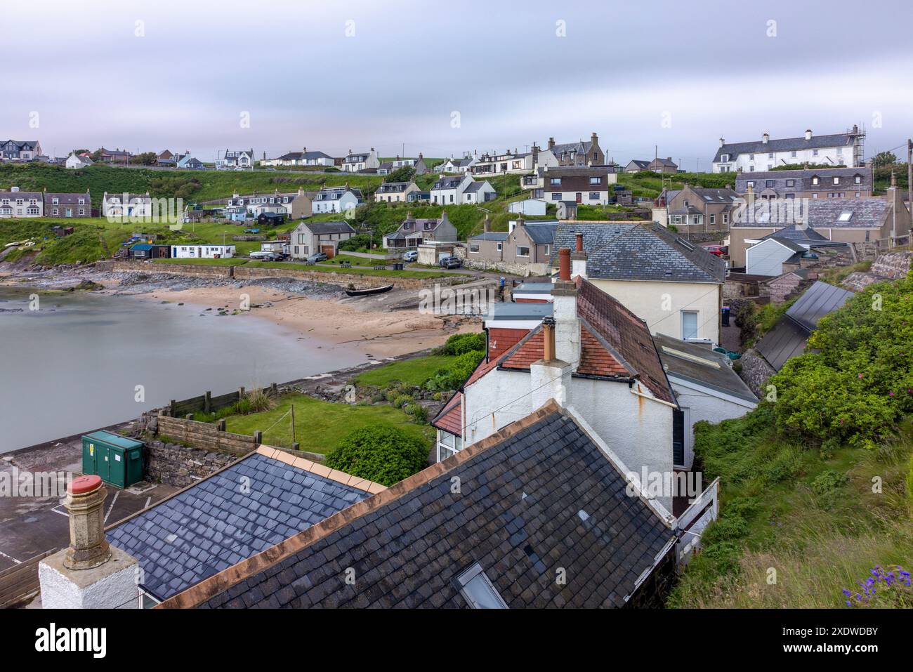 Il pittoresco Collieston Harbour nell'Aberdeenshire, Scozia, presenta affascinanti cottage annidati contro aspre scogliere, che si affacciano su un piccolo riparato Foto Stock