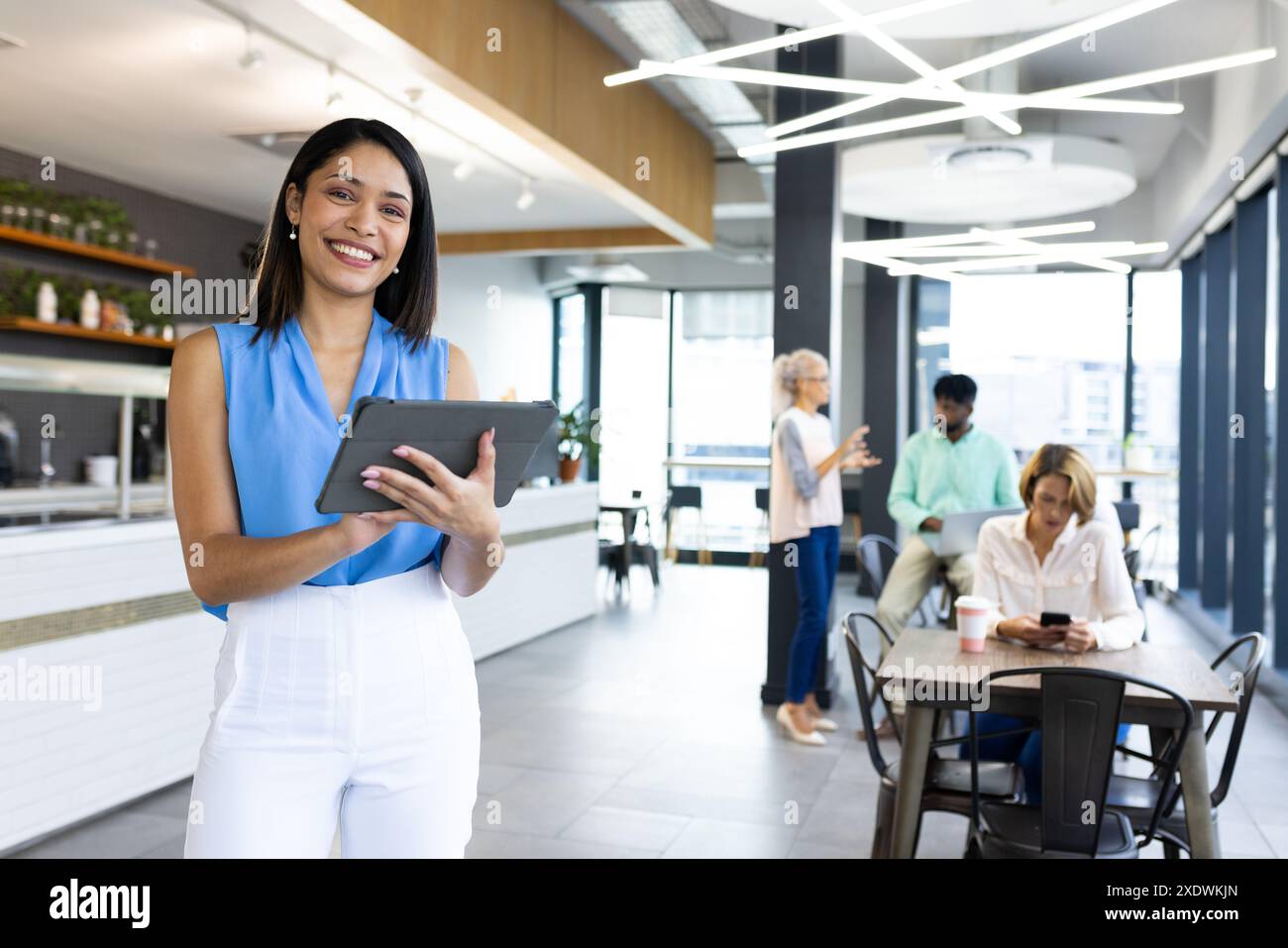 Tenere un tablet in un ufficio moderno, un professionista di sesso femminile con colleghi in background Foto Stock