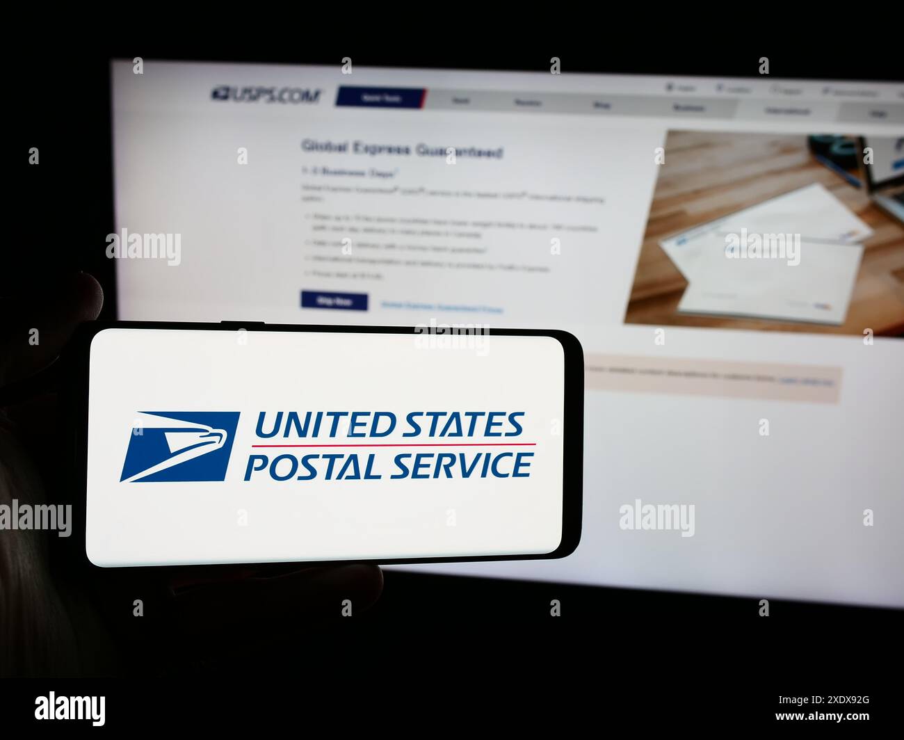Persona con smartphone con logo dell'agenzia statunitense USPS (United States Postal Service) davanti al sito Web. Mettere a fuoco il display del telefono. Foto Stock