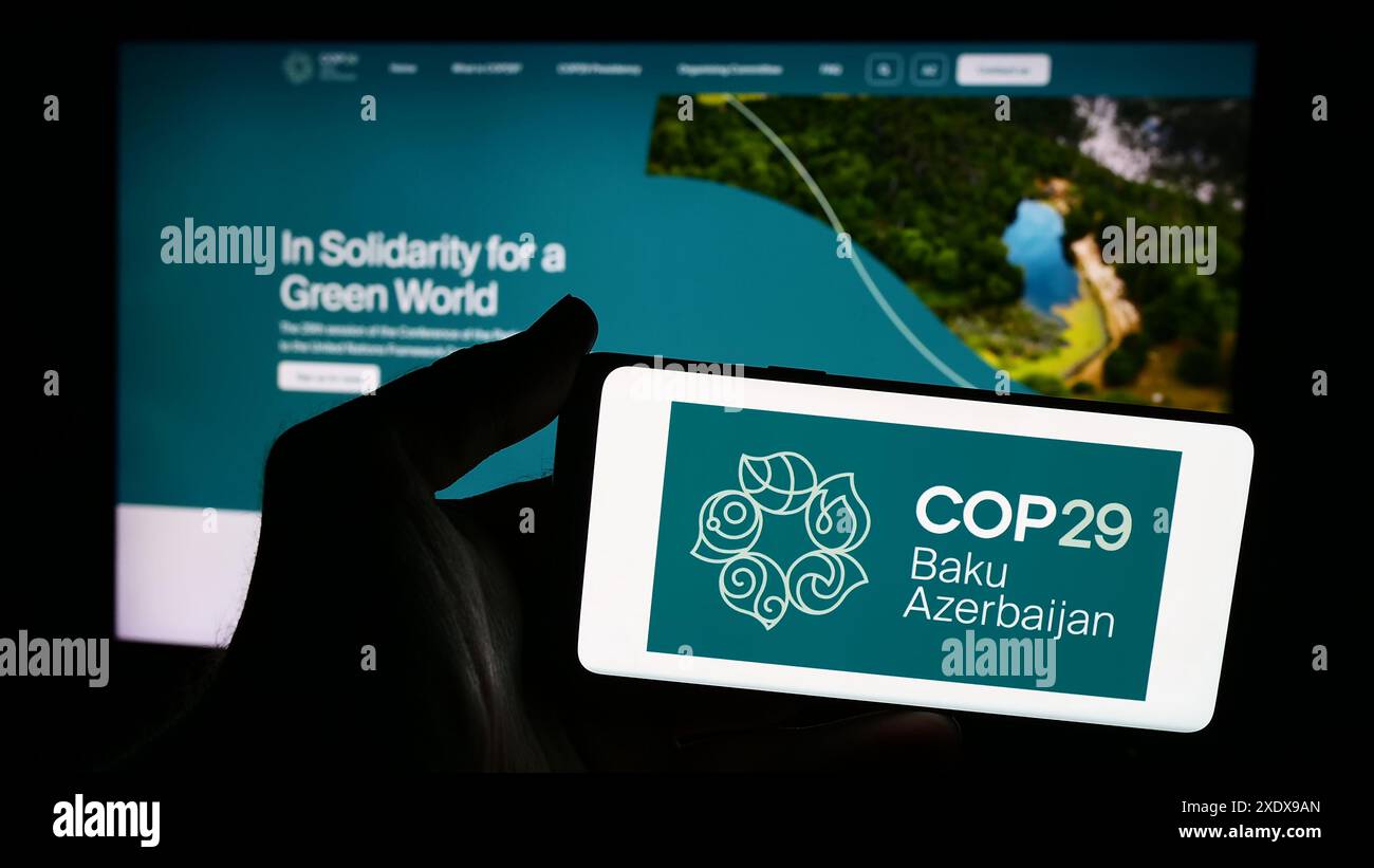 Persona che possiede uno smartphone con il logo della Conferenza delle Nazioni Unite sui cambiamenti climatici 2024 COP29 davanti al sito web. Mettere a fuoco il display del telefono. Foto Stock
