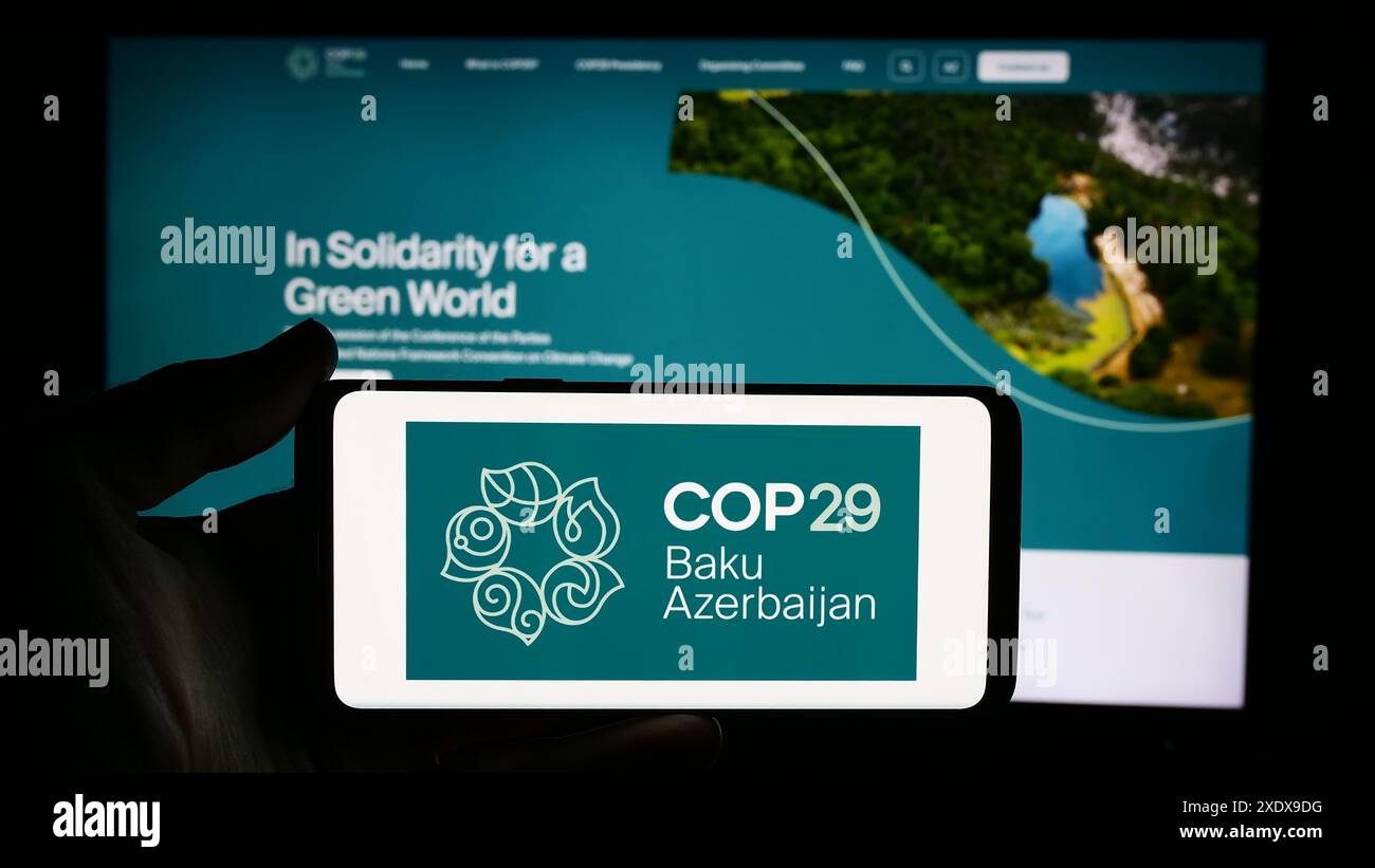 Persona che detiene un cellulare con il logo della Conferenza delle Nazioni Unite sui cambiamenti climatici 2024 COP29 di fronte alla pagina web. Mettere a fuoco il display del telefono. Foto Stock