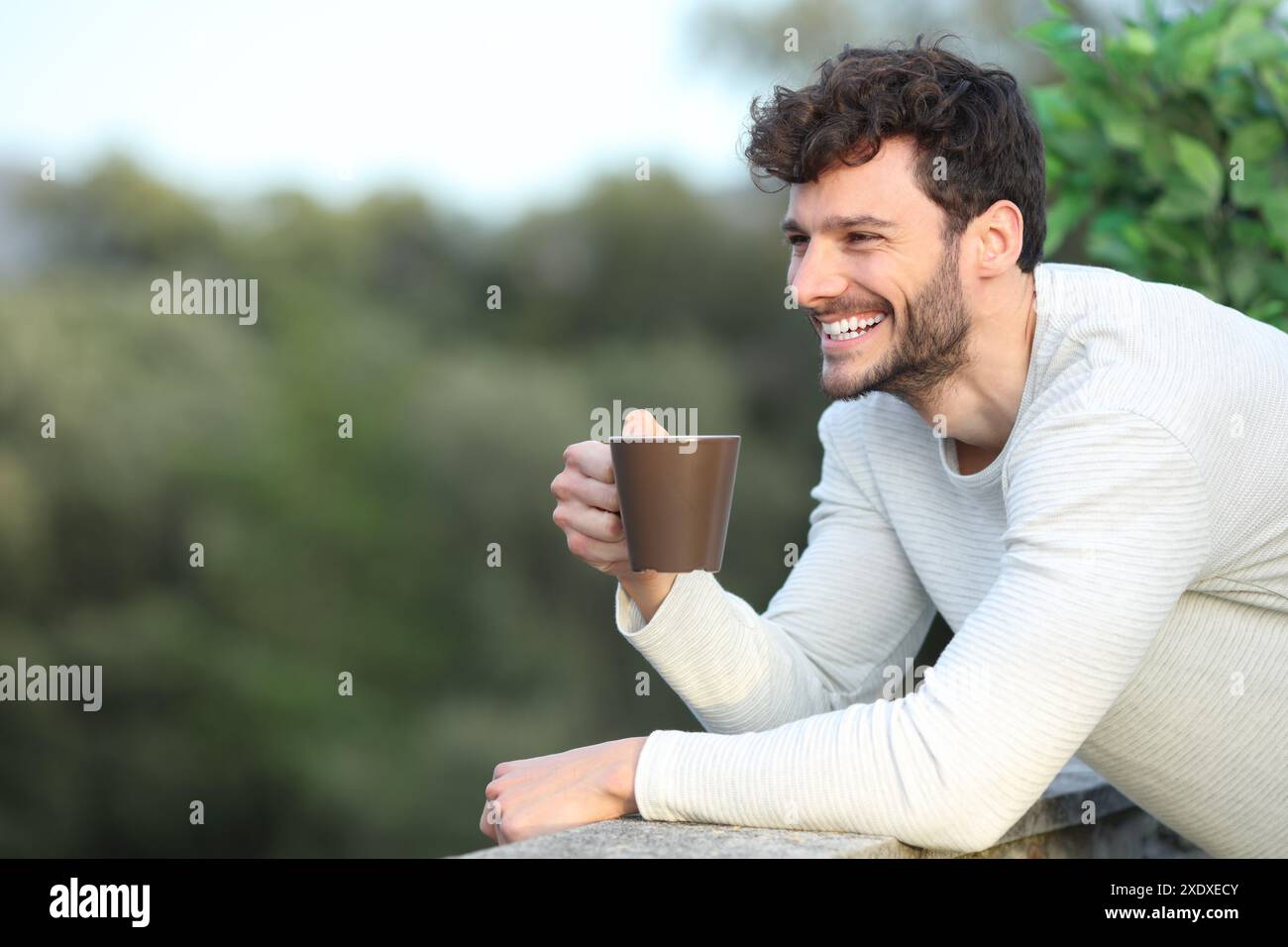 Uomo felice in una terrazza che beve caffè guardando lontano da casa Foto Stock