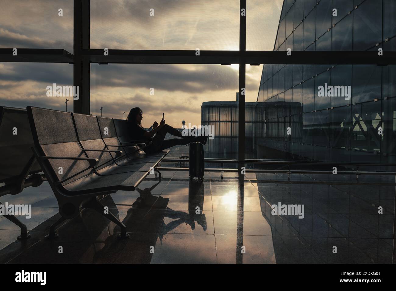 Una donna con i piedi in valigia controlla il cellulare mentre aspetta il volo nell'area d'imbarco dell'aeroporto. Foto Stock