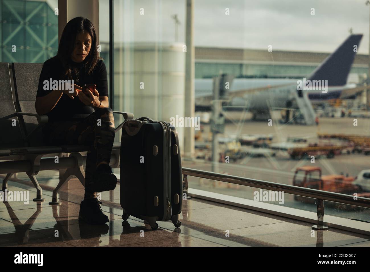 Una donna controlla il suo cellulare mentre aspetta il volo nell'area d'imbarco dell'aeroporto. Foto Stock