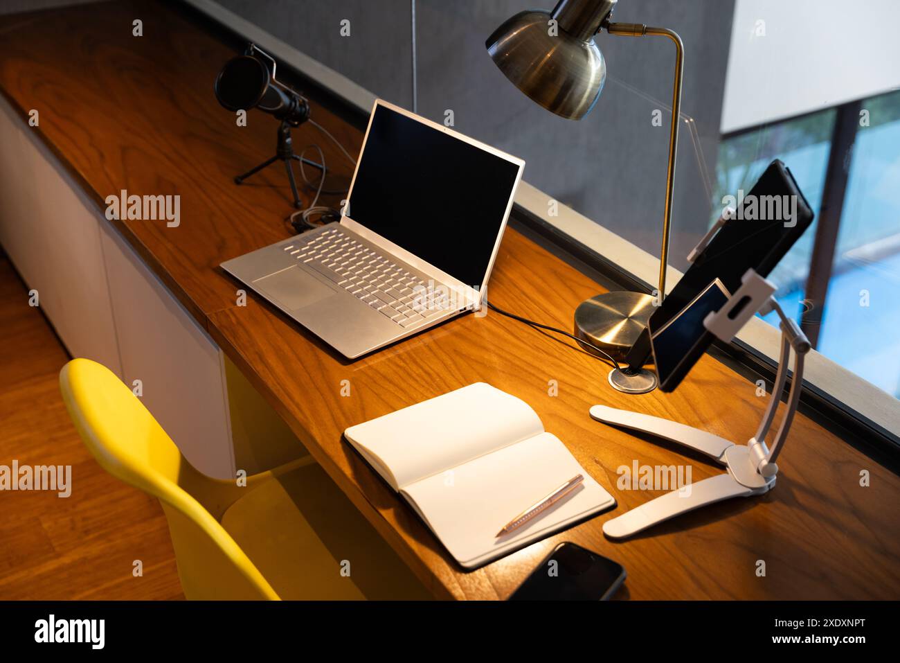 Configurazione dell'ufficio domestico con computer portatile, microfono, notebook e tablet su una scrivania in legno, spazio di copia Foto Stock