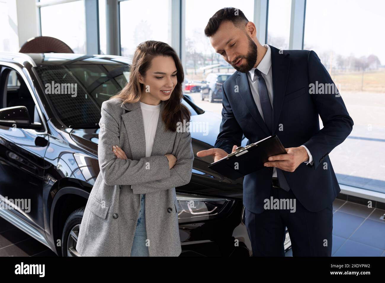 Un dipendente di un'officina prepara i documenti per una nuova auto per un acquirente donna Foto Stock