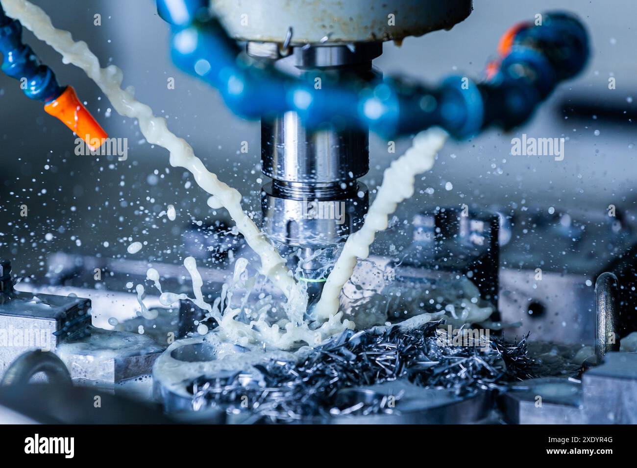 Un processo di fresatura verticale dell'acciaio cnc con flussi esterni di liquido di raffreddamento, schizzi e molti trucioli di metallo - primo piano con S. Foto Stock
