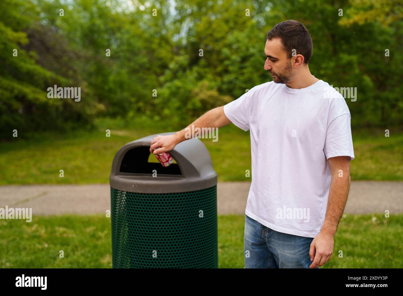 Uomo che cammina con rifiuti. Portare a mano il sacchetto di plastica contro i bidoni della spazzatura sulla strada. Foto Stock