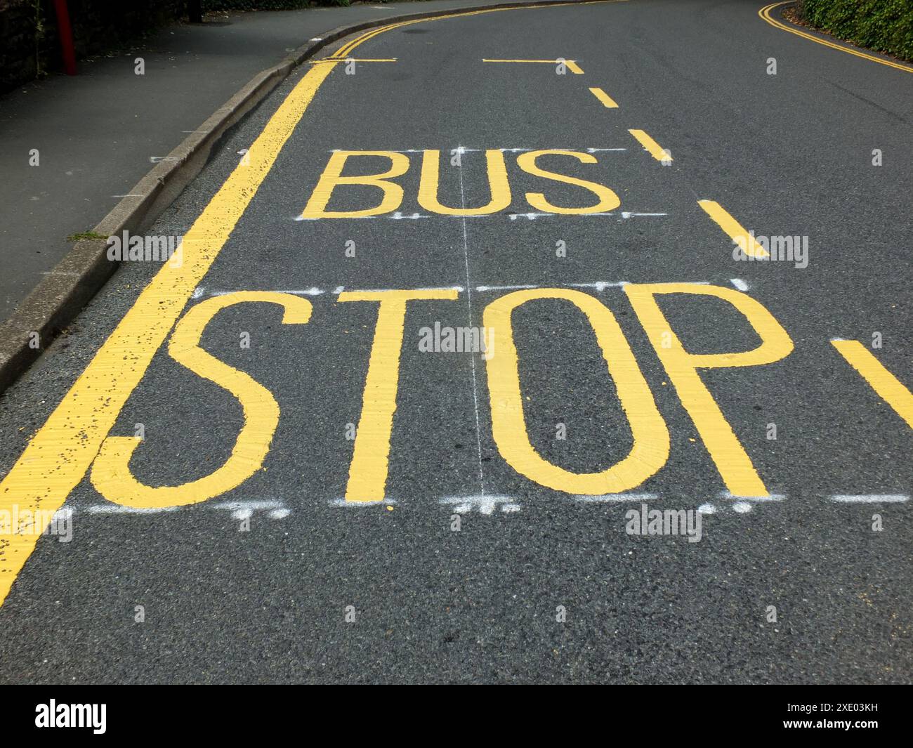 La fermata dell'autobus di colore giallo è stata recentemente dipinta e segnaletica su una stretta strada rurale asfaltata nera Foto Stock