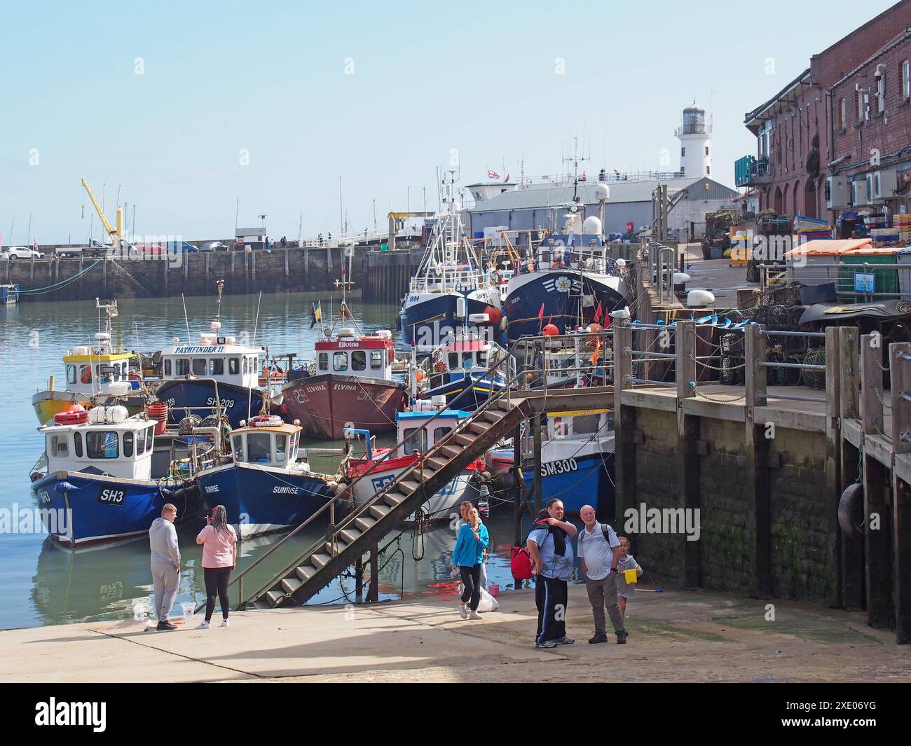 Turisti di fronte a pescherecci e pescherecci nel porto di Scarborough con edifici sul porto Foto Stock