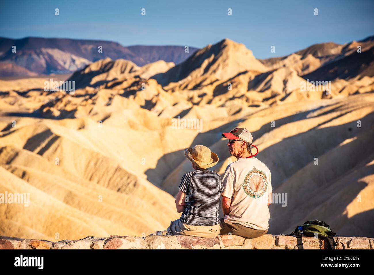 Coppia appollaiata su un muro di pietra a vista panoramica nel Parco Nazionale della Valle della morte con vista di Zabriskie Point nella catena montuosa di Amargosa. Foto Stock
