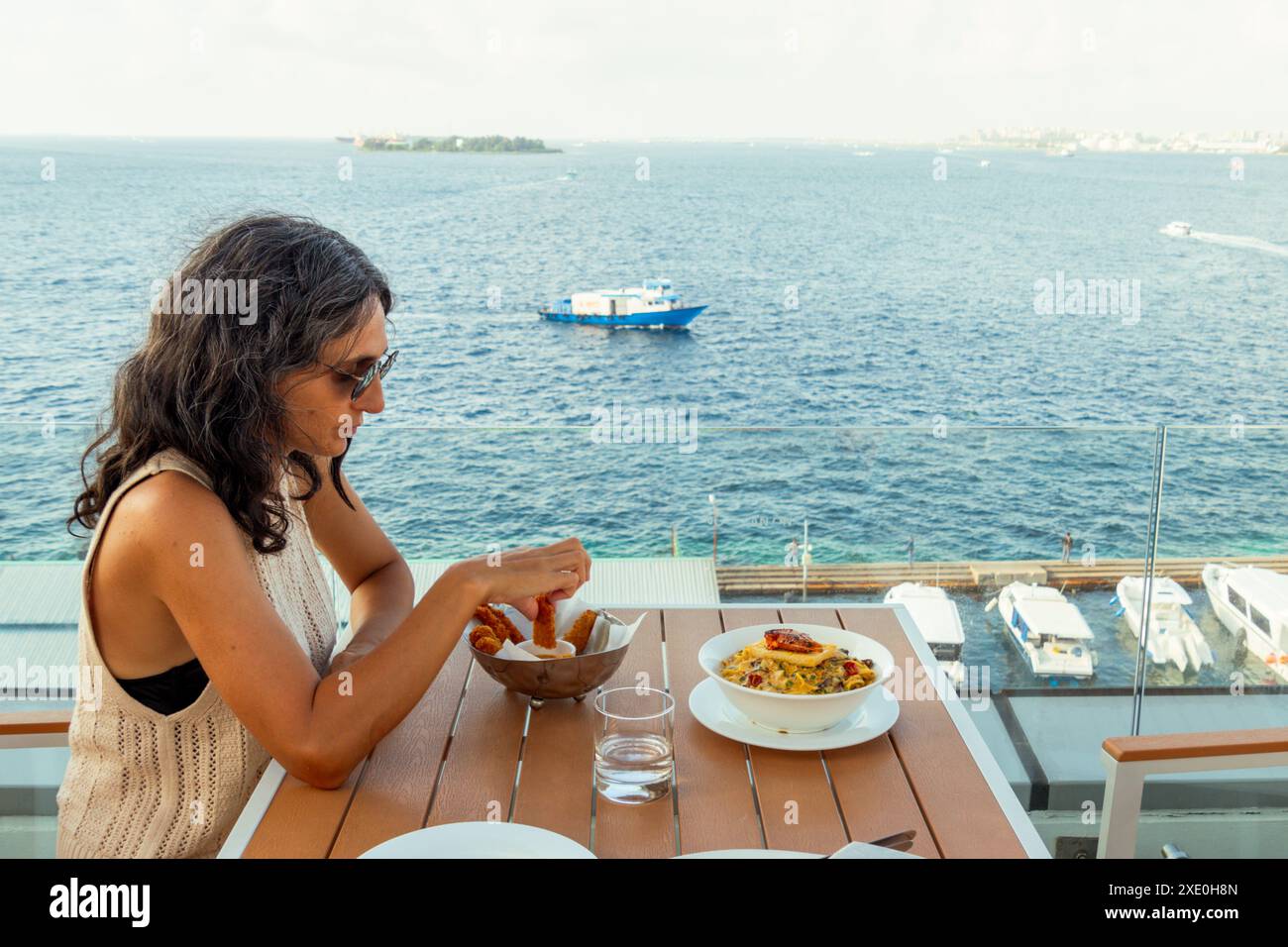 Male, Maldive - 10 maggio 2024: Turista caucasica siede al ristorante mangia tradizionale pesce fresco maschile godendo del panorama della costa Foto Stock