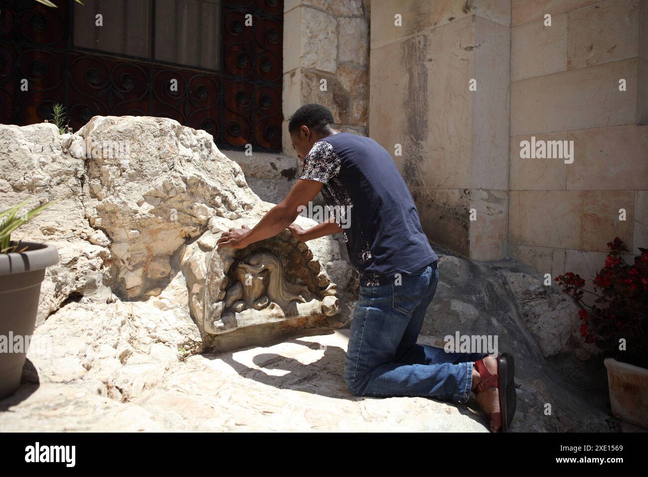 L'uomo nero nigeriano, un musulmano, convertito al cristianesimo pentecostale si inginocchia sulla roccia dell'Agonia nel Giardino del Getsemani, sta pregando e meditando Foto Stock