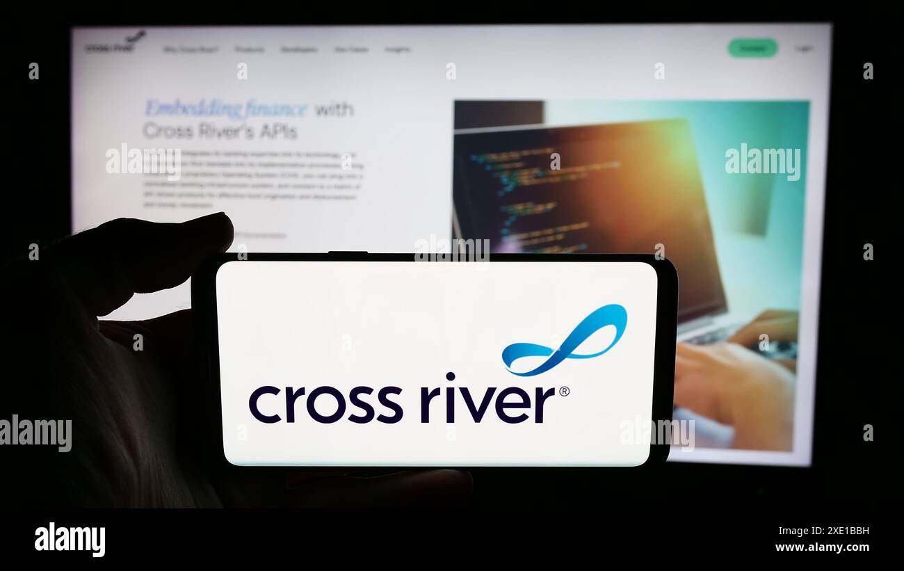 Persona che detiene un cellulare con il logo della società statunitense di servizi finanziari Cross River Bank di fronte alla pagina web aziendale. Mettere a fuoco il display del telefono. Foto Stock