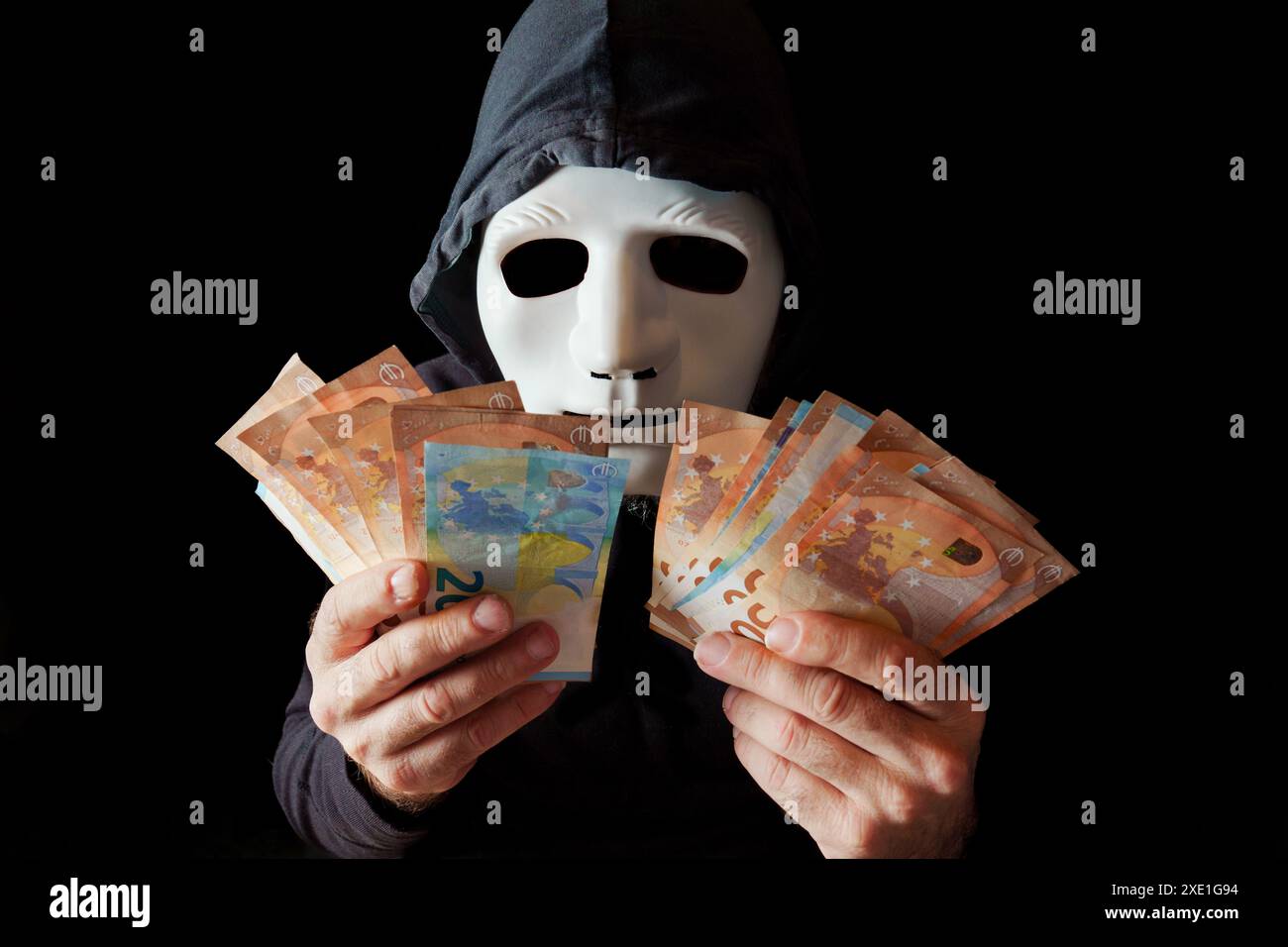 Hacker vestito di nero con maschera bianca e cappuccio nero che contano le banconote in euro Foto Stock