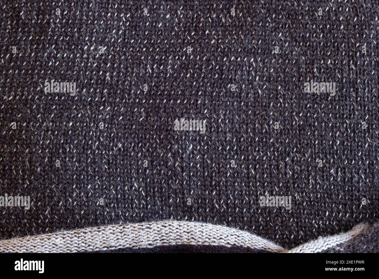 Il primo piano di un maglione con fili bianchi e grigi scuri crea una profondità monocromatica. Il bordo inferiore, con trama sparsa e finitura grezza. Foto Stock