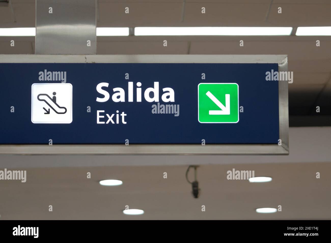 Cartello blu di uscita in un aeroporto, scritto in spagnolo e inglese. Foto Stock