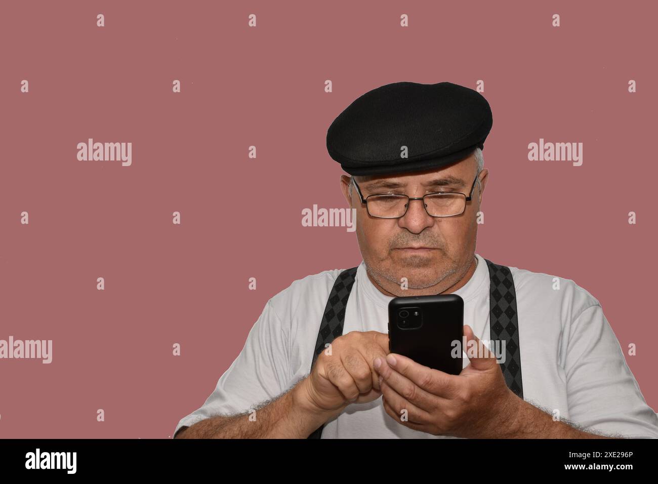 Ritratto di un uomo anziano con gli occhiali e un cappello che compone un numero su uno smartphone. Foto Stock