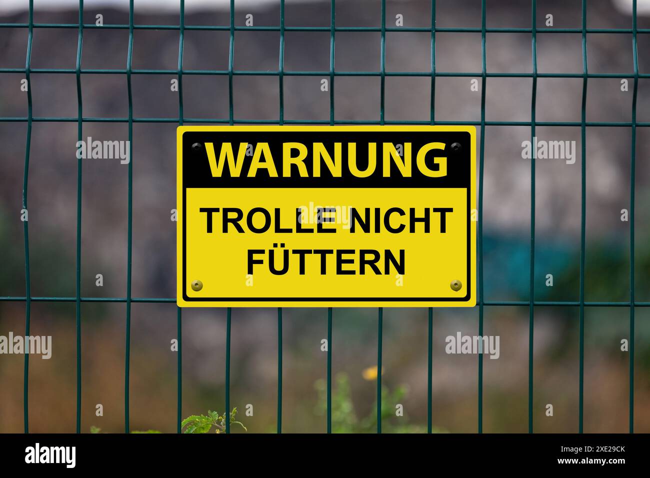 Cartello di avvertimento giallo su una recinzione che recita in tedesco: "Warnung - trolle nicht füttern", che in inglese significa "attenzione - non dare da mangiare ai troll". Foto Stock