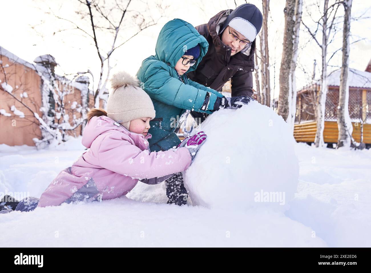 Una famiglia costruisce un pupazzo di neve bianca nel cortile in inverno. Foto Stock