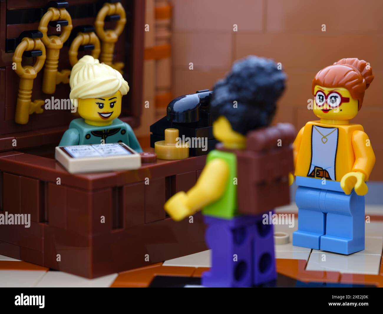 Tambov, Federazione Russa - 21 giugno 2024, Una minifigura della receptionist Lego in piedi dietro il tavolo del ricevimento in un hotel e che parla con gli ospiti dell'hotel Foto Stock