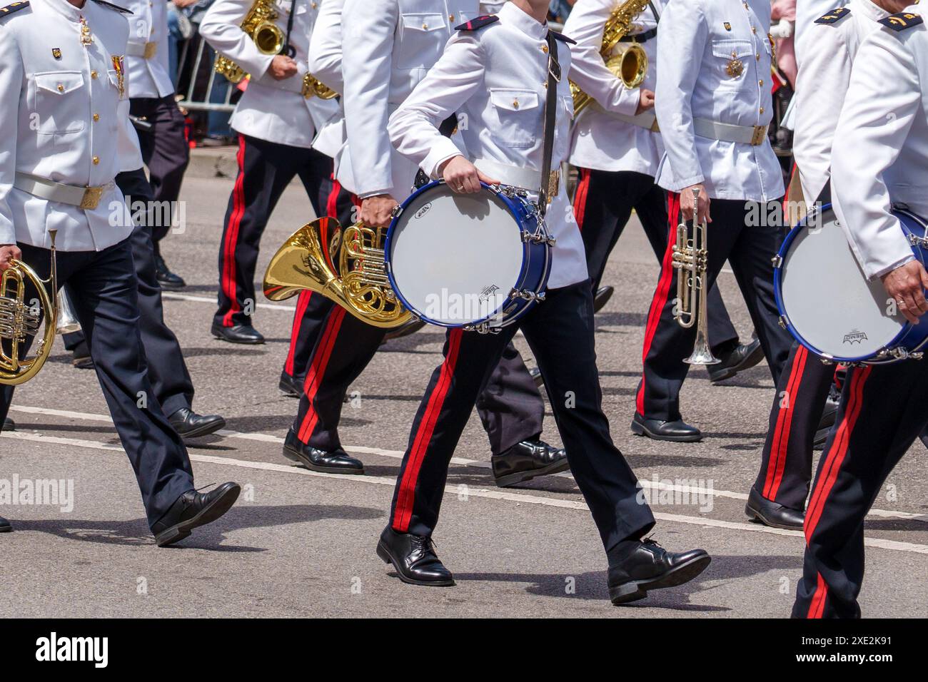 Oviedo, Spagna - 25 maggio 2024: Una banda militare in marcia con batteria e strumenti musicali in ottone in uniforme bianca con strisce rosse sui pantaloni neri mar Foto Stock