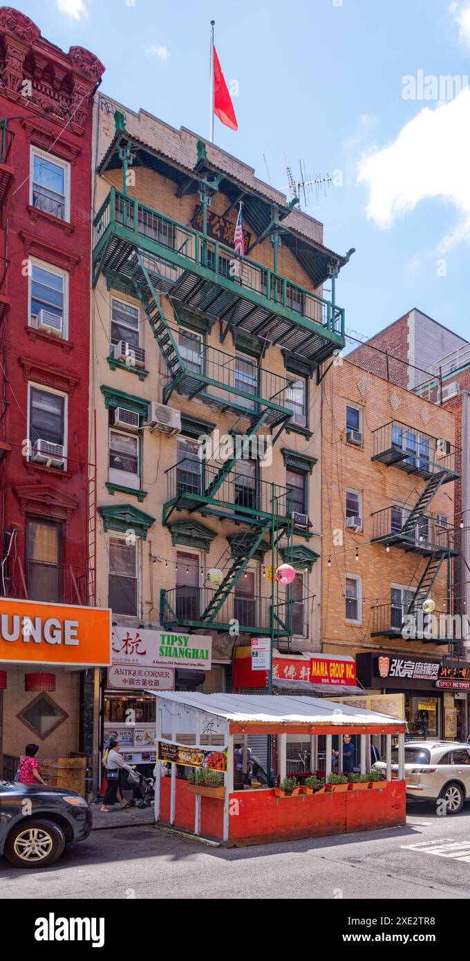 NYC Chinatown: Una bandiera cinese vola sopra 68 Mott Street, un edificio di appartamenti a cinque piani in mattoni, e negozi, con un balcone coperto all'ultimo piano. Foto Stock